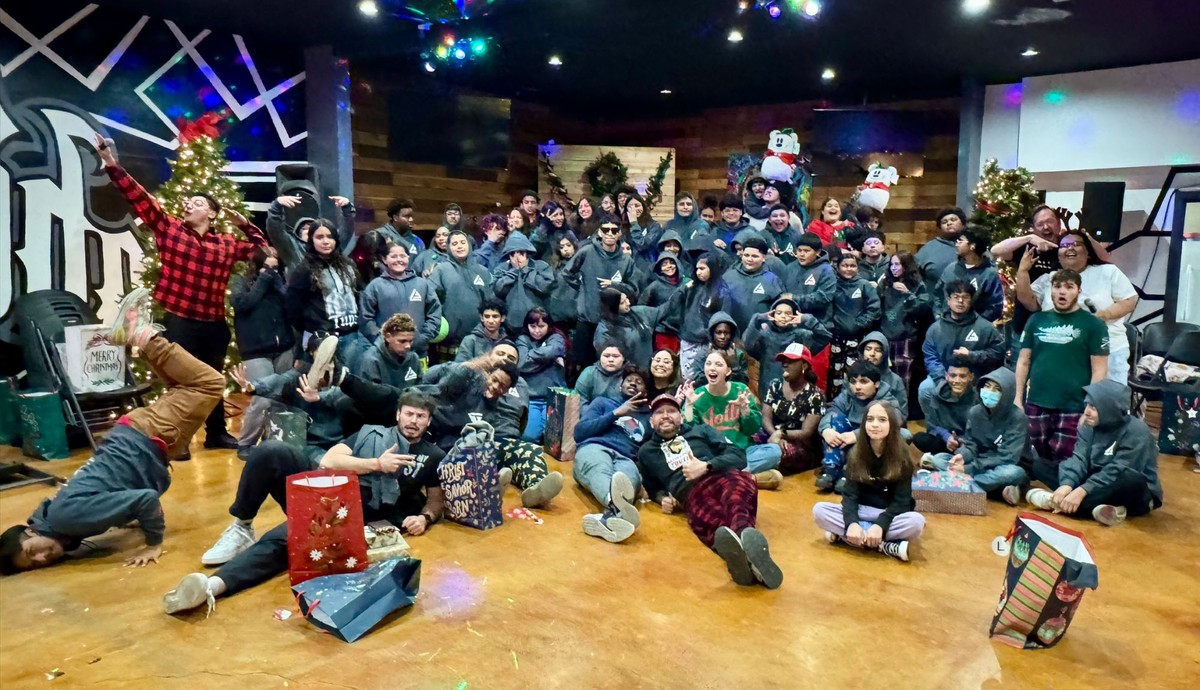 A large group of AGORA youth in matching hoodies at a Christmas party, laughing and posing on the floor